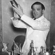 Black-and-white photo of barkeep in suit shaking cocktail in shaker